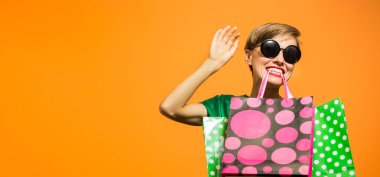 Holding alışveriş çantası turuncu arka plan üzerinde alışveriş yeşil elbiseli güzel beyaz kadın