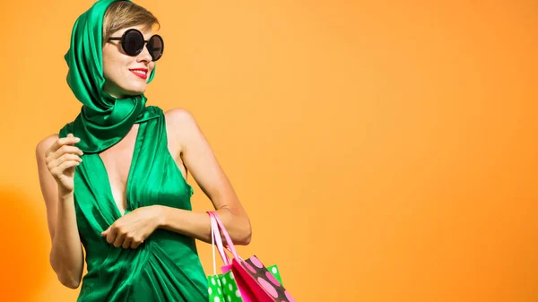 オレンジ色の背景で持株ショッピング バッグをショッピングの緑のドレスで美しい白人女性 — ストック写真