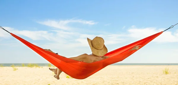 Relaxed woman lying in a hammock with the view of blue sky and sea line