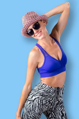 Mavi arka plan üzerinde şapka ve güneş gözlüğü güzel kadın