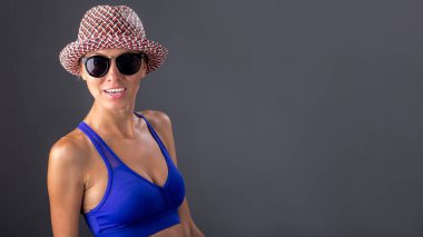 Güzel sarışın kadın yaz şapka, mayo ve güneş gözlüğü giyen ve eğlenceli iyi bir ruh hali vardır