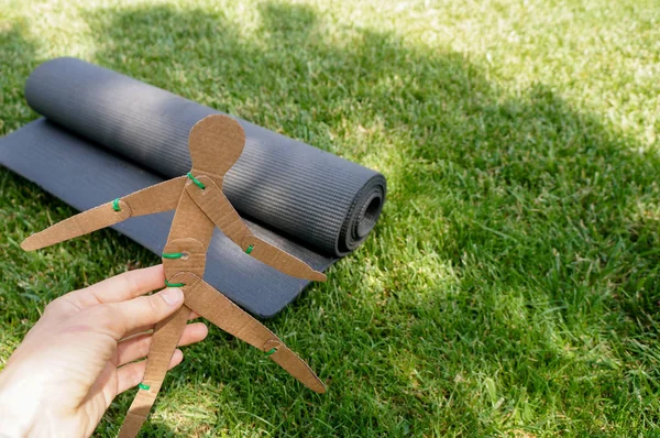 Yoga day concept. Paper man stretching near yoga mat on green lawn