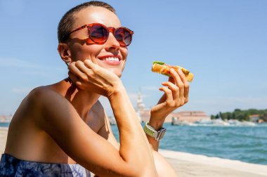 Güneşli bir yaz gününde Venedik manzarası ile sandviç yiyen mutlu genç beyaz kadın