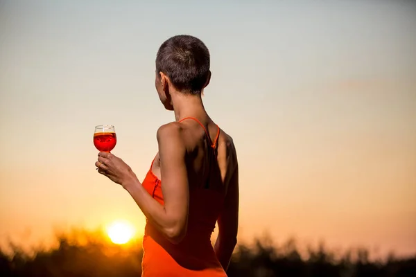 Woman with a cocktail over suset sky in orange colors.