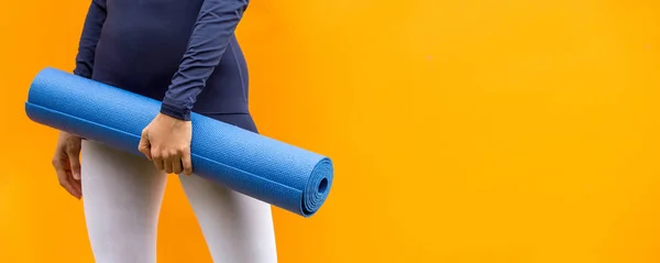 Sporty yoga girl with yoga mat wearing sport clothes over orange background