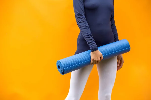 Sporty yoga girl with yoga mat wearing sport clothes over orange background