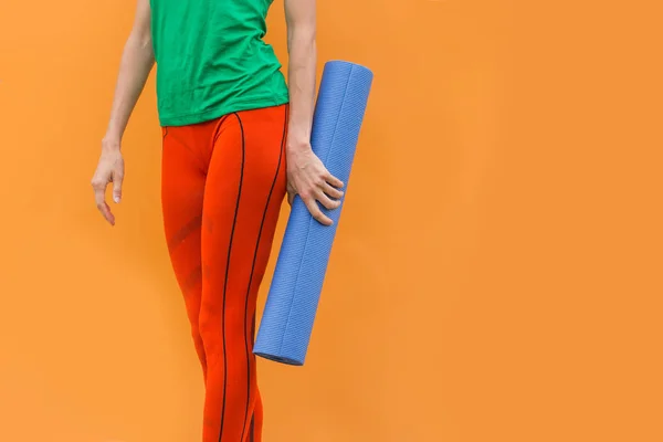 オレンジ色の背景の上にスポーツ服を着てヨガマットとスポーティなヨガの女の子 — ストック写真