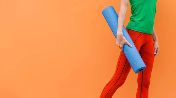 Sporty yoga girl with yoga mat wearing sport clothes over orange background