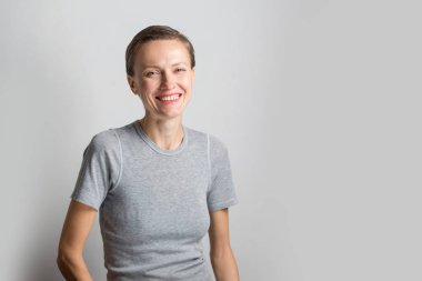 Kısa saçlı, neşeli genç bir kadın açık gri arka planda doğal makyaj yapıyor. Güzel, esmer, neşeli gülümseyen genç bir kadının kapalı bir portresi.