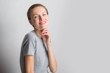 Kısa saçlı, neşeli genç bir kadın açık gri arka planda doğal makyaj yapıyor. Güzel esmer bir kadının kapalı bir portresi neşeyle gülümsüyor.