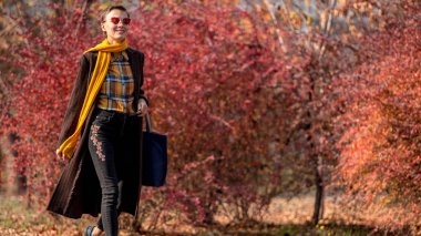  Güz parkında son moda sonbahar kıyafetli şık bir sonbahar kadını yürüyor.