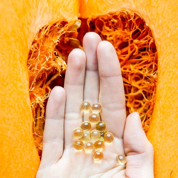 Woman health pill in a palm over an orange cut on halves pumpkin