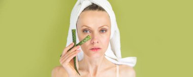 Yeşil aloe vera yaprağı tutan beyaz tenli genç bir kadının portresi