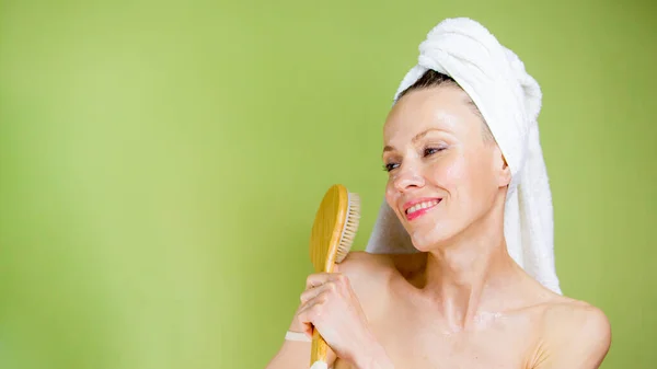 young woman in towel in bathroom holding massage brush over green olive background