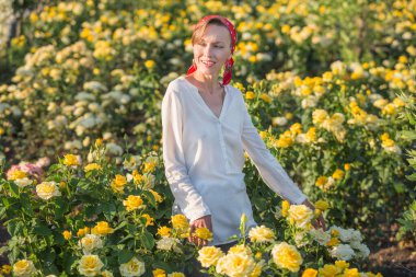 Kırmızı başörtüsü takan güzel bir kadın, beyaz bluz çiçekli tarlada duruyor.