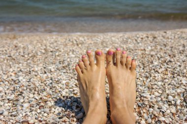 Tatil tatili. Kadının ayakları, güneşli yaz günlerinde sahilde güneşlenen bir kızın yakın çekimi.