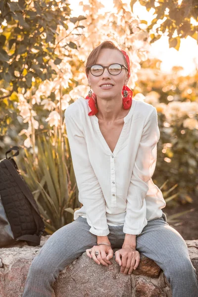 Happy cheerful young woman with natural makeup  wearing white blouse, red scarf on head and grey panrts, natural and cheerful young woman relaxing and enjoying sunny day