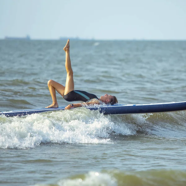 Woman practicing yoga on the paddle board in the morning on a wavy sea