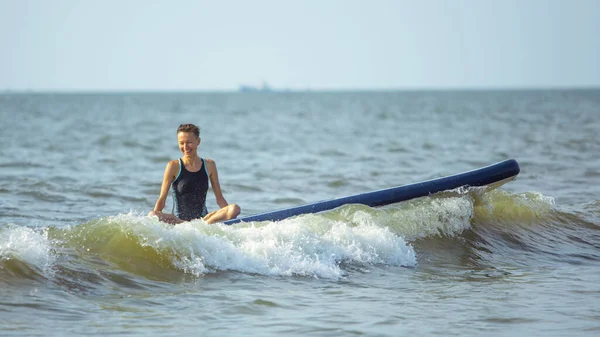 Woman practicing yoga on the paddle board in the morning on a wavy sea