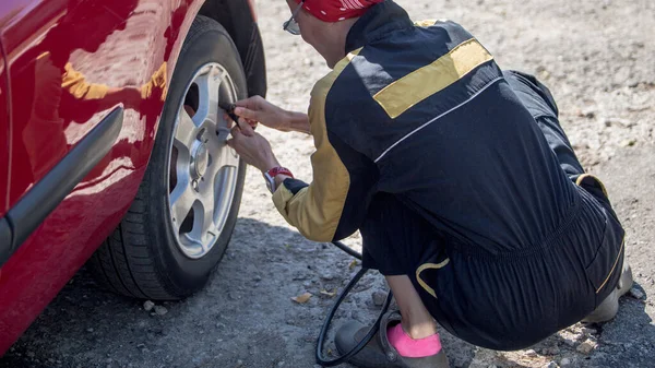 Female mechanic inflating tire and checking air pressure with gauge pressure by herself. Woman at work concept