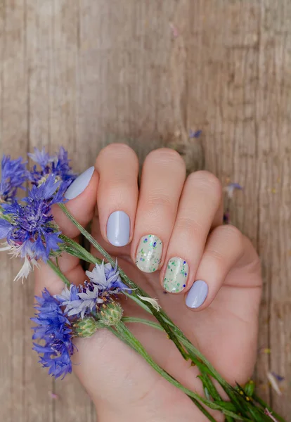 Female hands with blue nail design holding blue flowers.