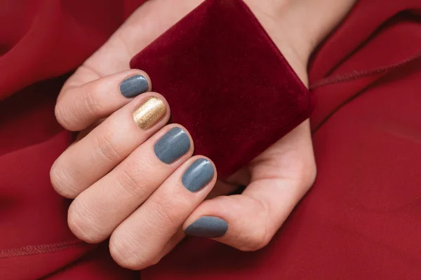 Female hand with blue nail design holding red gift box — Stock Photo, Image