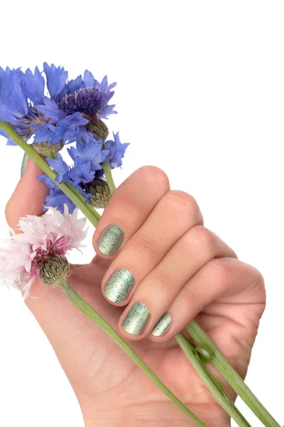 Main féminine avec motif ongle vert tenant des fleurs bleues . — Photo