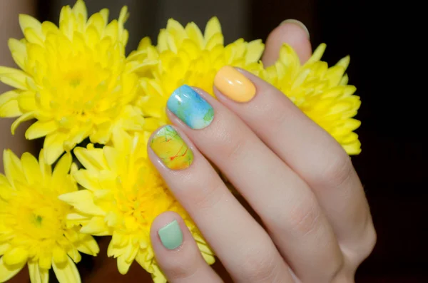 Main féminine avec motif d'ongles jaunes tenant fleur jaune — Photo