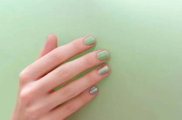 Female hand with green nail design on green background