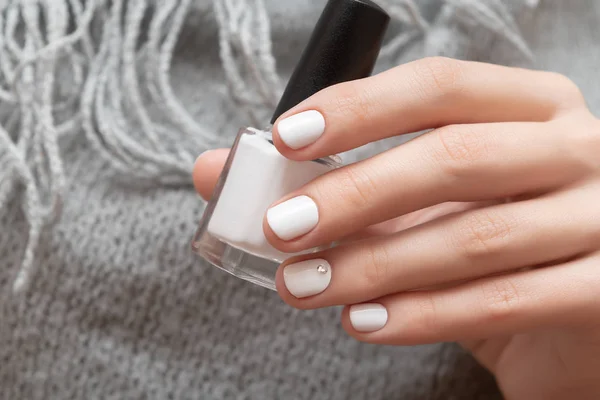 Mano femenina con diseño de uñas blancas sosteniendo botella de esmalte de uñas . — Foto de Stock
