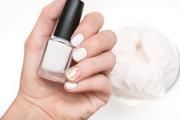 Female hand with white nail design holding nail polish bottle. — Stock Photo, Image