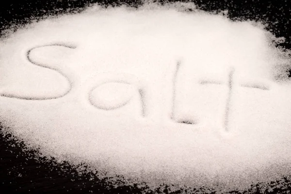 Salt written on spilled salt on black background — Stock Photo, Image
