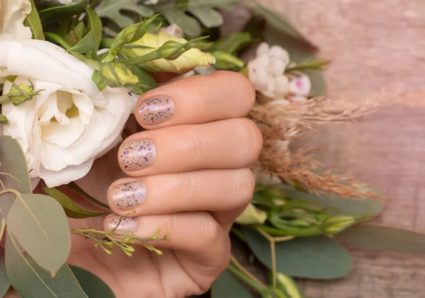 Mão feminina com design de unhas glitter segurando flores — Fotografia de Stock