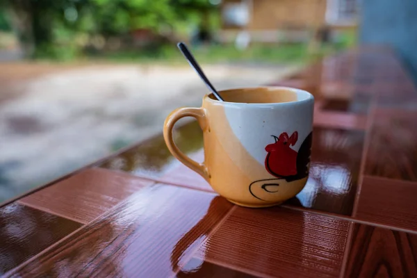 Uma xícara de café latte em copo branco na mesa de azulejos com cadeiras borradas no fundo — Fotografia de Stock