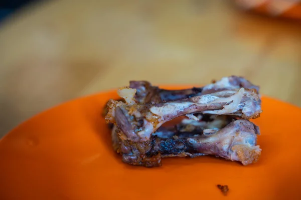 Osso di pollo su un piatto arancione con sfondo in legno sfocato — Foto Stock