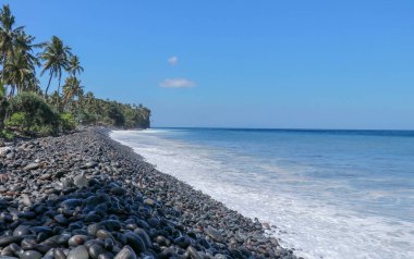 Siyah çakıl taşlı tropik plaj. Kayalık bir sahili olan Bali adası. siyah kumsal Endonezya