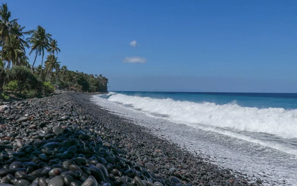 Trópusi strand fekete kavicsokkal. Bali szigete sziklás parttal. fekete homokos strand Indonézia — Stock Fotó