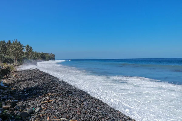Tropical beach with black pebbles. The island of Bali with a rocky coast. black sand beach Indonesia