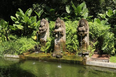 Bali Endonezya 'da arka planda orman olan bir çeşmenin üç heykeli. Suyun aktığı bir tencereyle balerin heykelciği. Havuz dekorasyonu.
