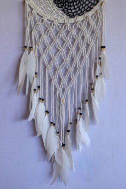 Kayaların ve gölün arka planında beyaz altlıklı el yapımı pembe rüya yakalayıcı. Kabile elementleri, tüyler, dantel, tığ işi kar tanesi.