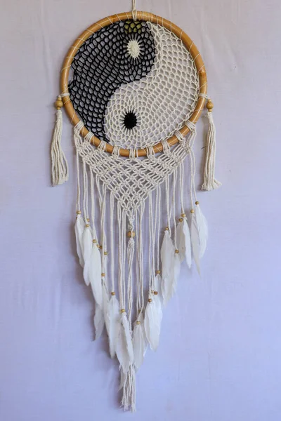 Dream catcher, decorated with white feathers and wooden beads, on a wooden surface. Dream catcher with wooden circle. Knitted Native American amulet with the symbol of Yin Yang on a white background.