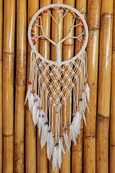 Dream catcher, decorated with white feathers and wooden beads, on a wooden surface. Dream catcher with wooden circle. Knitted Native American amulet with the symbol of Yin Yang on a wodden background.