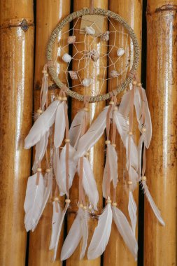Deniz kabuğu süslemesi. Düş kapanı. Kayaların ve gölün arka planında el yapımı pembe Amerikan Yerlisi rüya yakalayıcısı. Kabile elementleri, tüyler, kabuklar, dantel