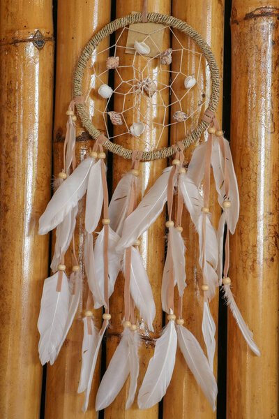 sea shell decoration. dream catcher. Handmade pink native american dream catcher on background of rocks and lake. Tribal elements, feathers, shells, lace