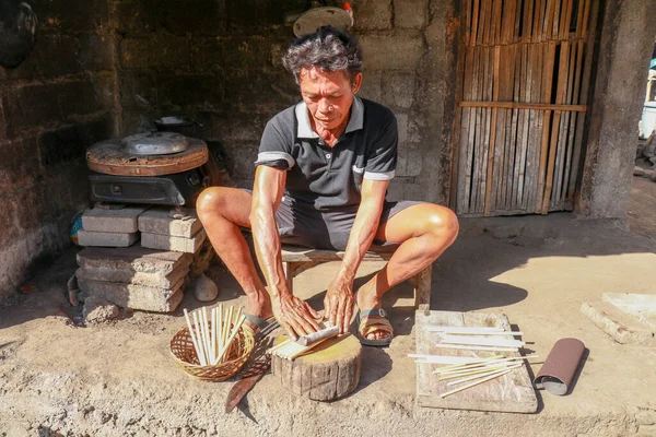 Old man working with bamboo in his workshop to make bamboo straws, Bali, Indonesia. Ecological way of producing recyclable products. Front view to a worker who makes bamboo straws