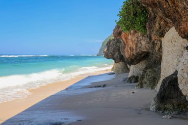 Dalgalar, Barbados 'un kumlu kıyı şeridinde uzanan büyük siyah bir kayaya çarpar ve gökyüzüne doğru yükselir. Turkuaz okyanus dalgaları Karayipler 'deki uzak bir tropik adanın kıyısına çarpar..