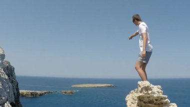 Genç gezgin ellerini dağın tepesinde güzel manzaranın üzerinde kaldırdı. Kaptan Süvarisi 'nin uçurumunda genç bir adam denize bakıyor ve elini uzatıyor, Menorca, İspanya.