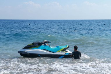 Mavi deniz suyunda yüzen Jetski. Güçlü su araçları müşterileri bekliyor. Genç Endonezyalı kıyıya yakın bir jet motoru tutuyor..