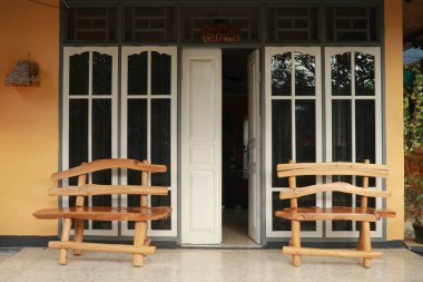 Evin beyaz camlı ahşap kapısı. Kapının kenarlarında ahşap banklar var. Bir evin ahşap kapısı. Yarı açık kapının önü. Yatay çekim.