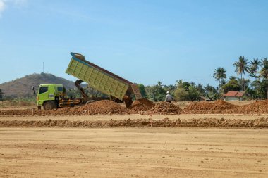 Yeşil damperli kamyon inşaat için kilini inşaat alanına boşaltıyor. Moto GP Mandalika yarış pisti yapım aşamasında, Lombok, Endonezya. Nakliye endüstrisi, kargo taşımacılığı.